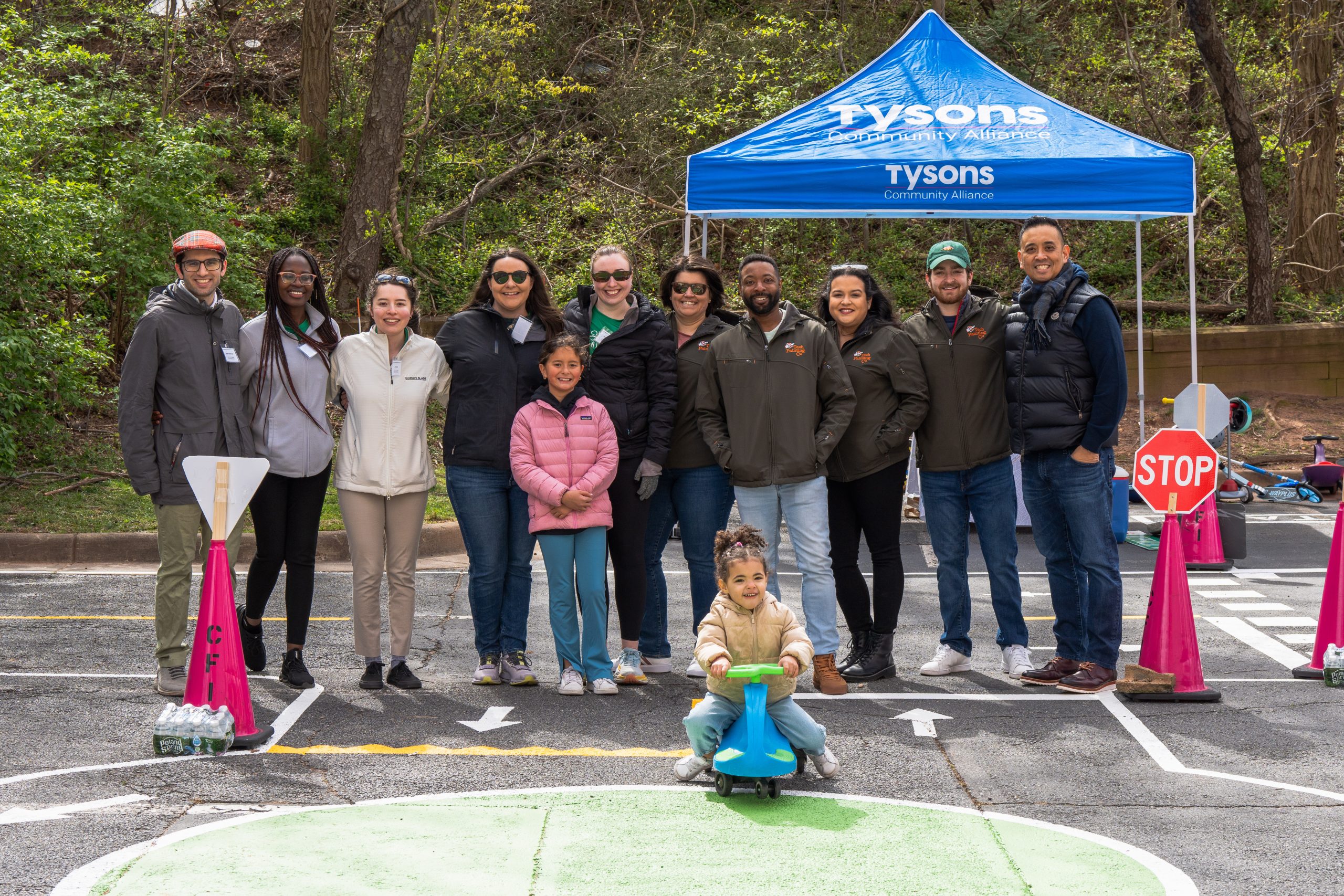 a group of adults stand in front of a blue tent with a toddler in front of them exploring the mobility maze